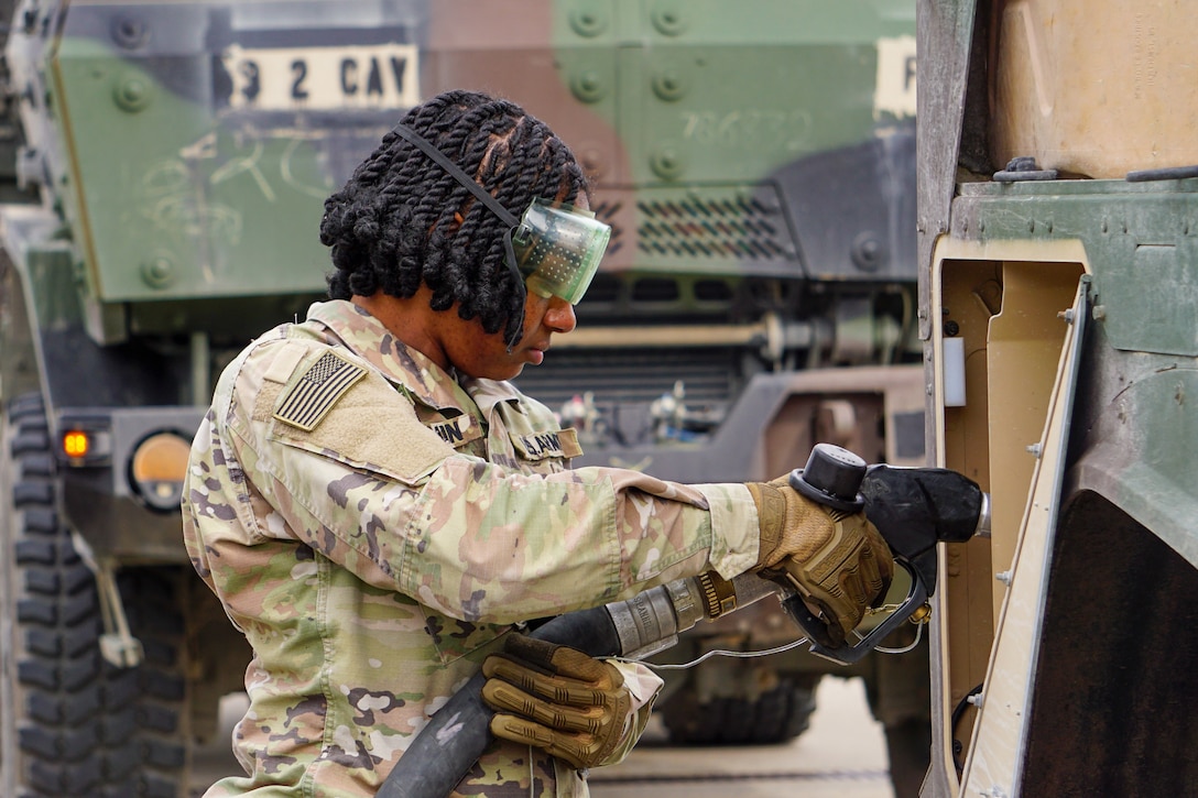A soldier wearing goggles and gloves puts fuel in a vehicle.