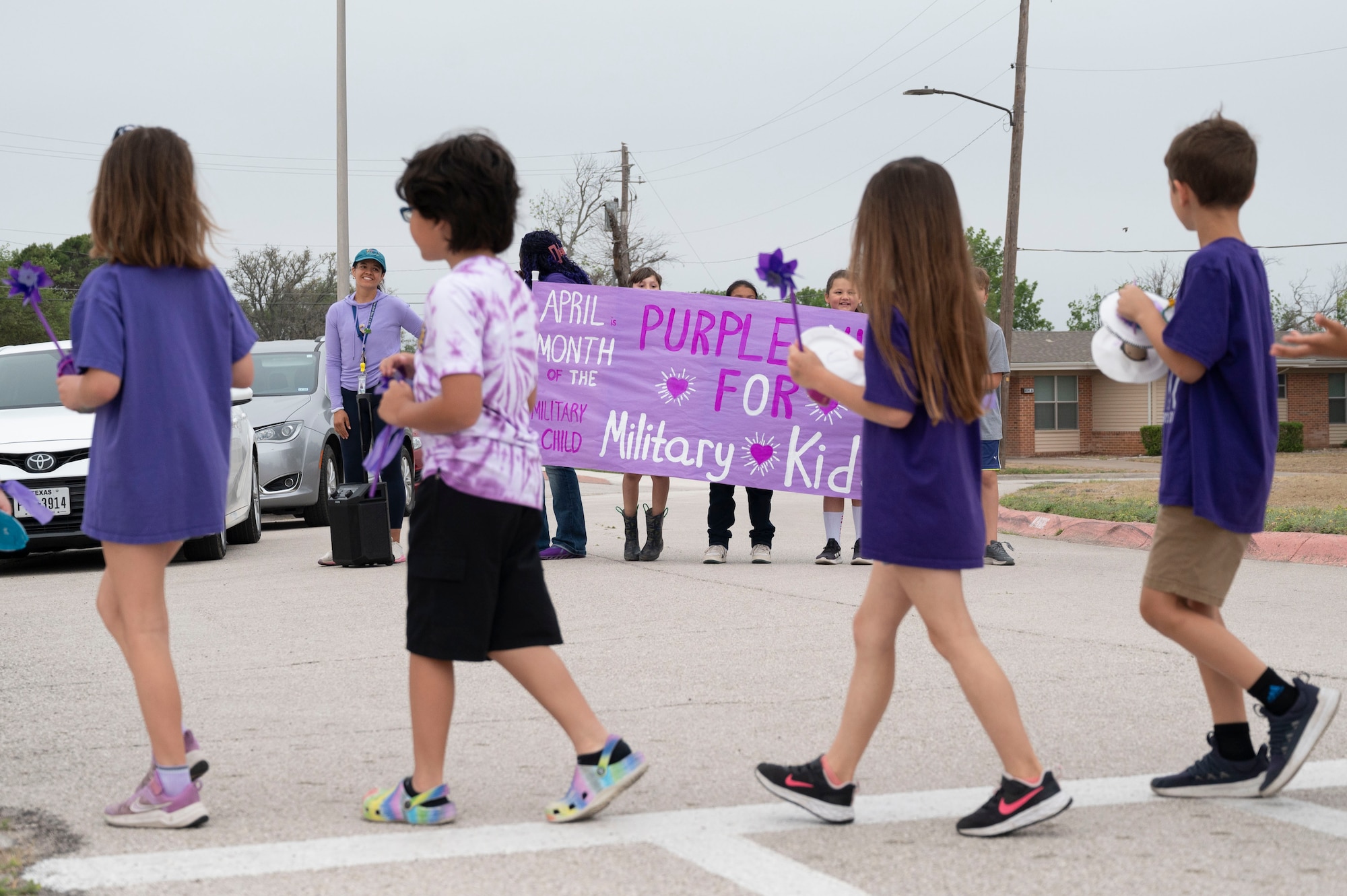 Staff and students from the Roberto “Bobby” Barrera (RBB) Elementary School hold up a Purple Up Day sign showcasing support while students walk the “Purple Up Parade” held at Laughlin Air Force Base, Texas, April 17, 2024. This parade was dedicated to celebrating Purple Up Day, a day devoted to showing support and appreciation for military children. (U.S. Air Force photo by Senior Airman Kailee Reynolds)