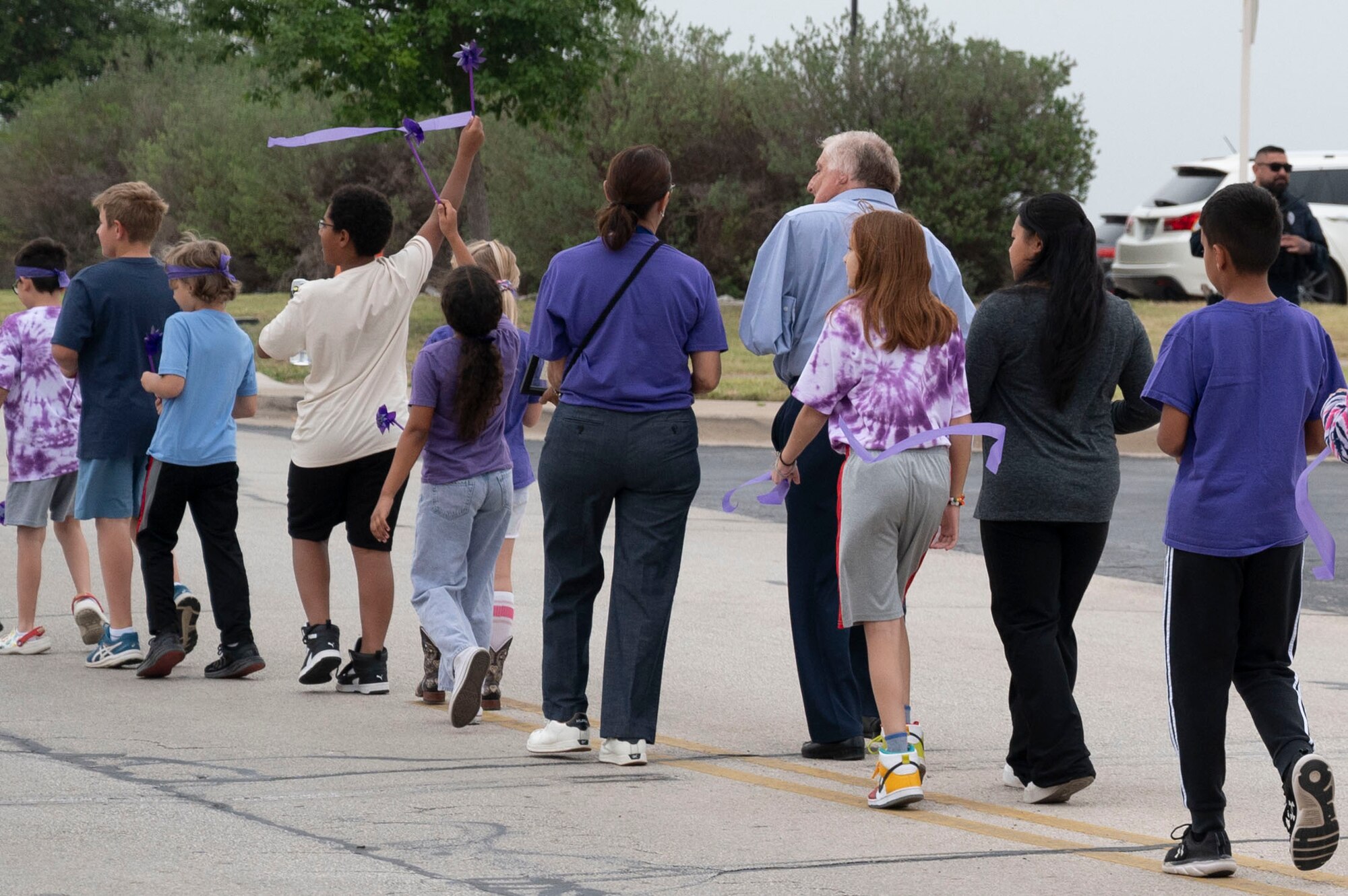Staff and students from the Roberto “Bobby” Barrera (RBB) Elementary School walk the “Purple Up Parade” alongside Roberto Barrera (blue shirt), U.S. Marine Corp. veteran and former educator, whom the school was named after, held at Laughlin Air Force Base, Texas, April 17, 2024. This parade was dedicated to celebrating Purple Up Day, a day devoted to showing support and appreciation for military children. (U.S. Air Force photo by Senior Airman Kailee Reynolds)