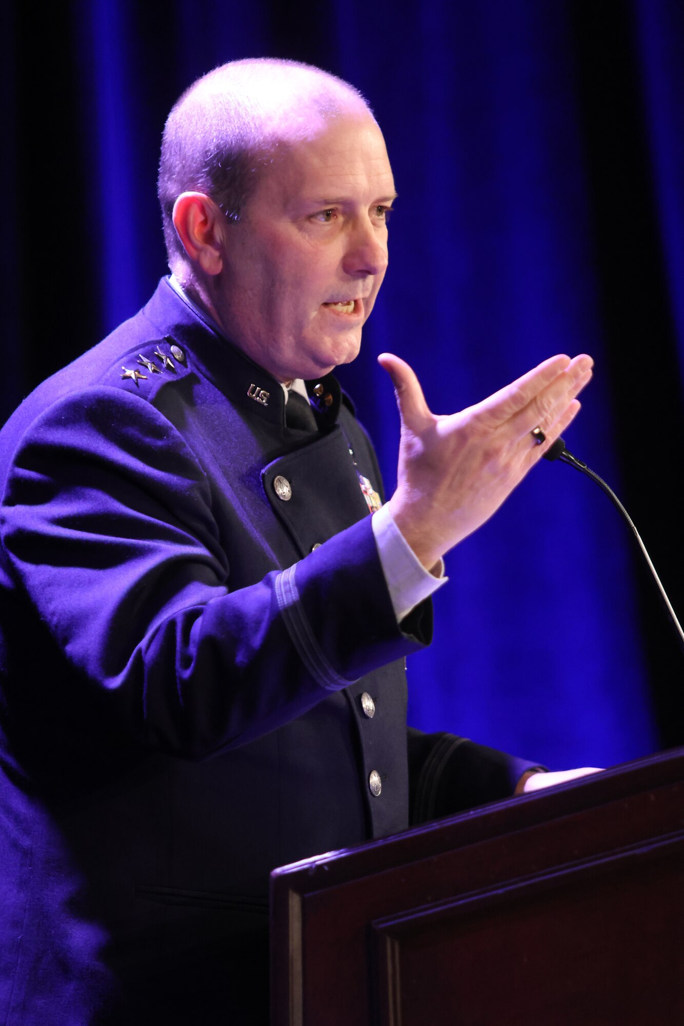 man speaking at podium with hand up
