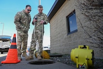 Two people standing next to a manhole with a tube going into the manhole