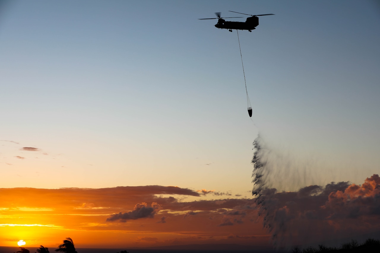 A helicopter flies with a water bucket attached.
