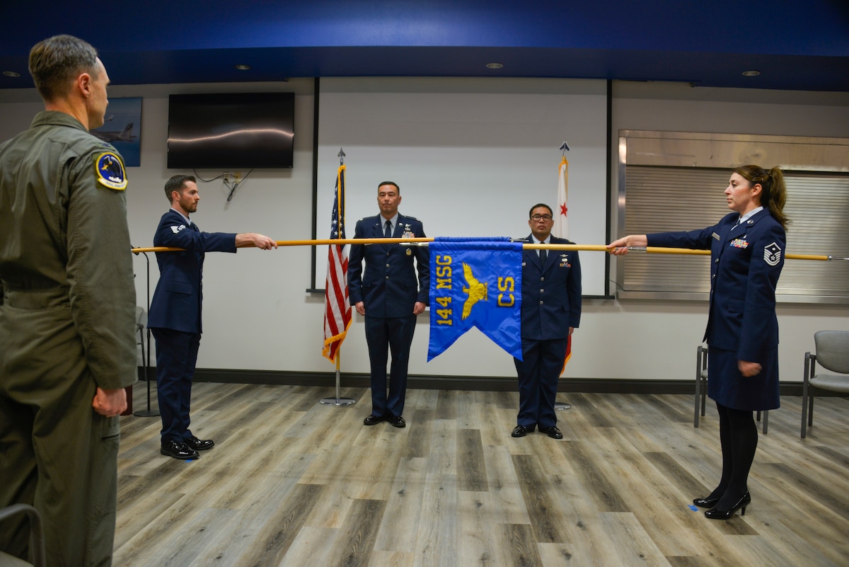 Two Airmen who are facing each other are holding guidons horizontally with one flag in front of the other.