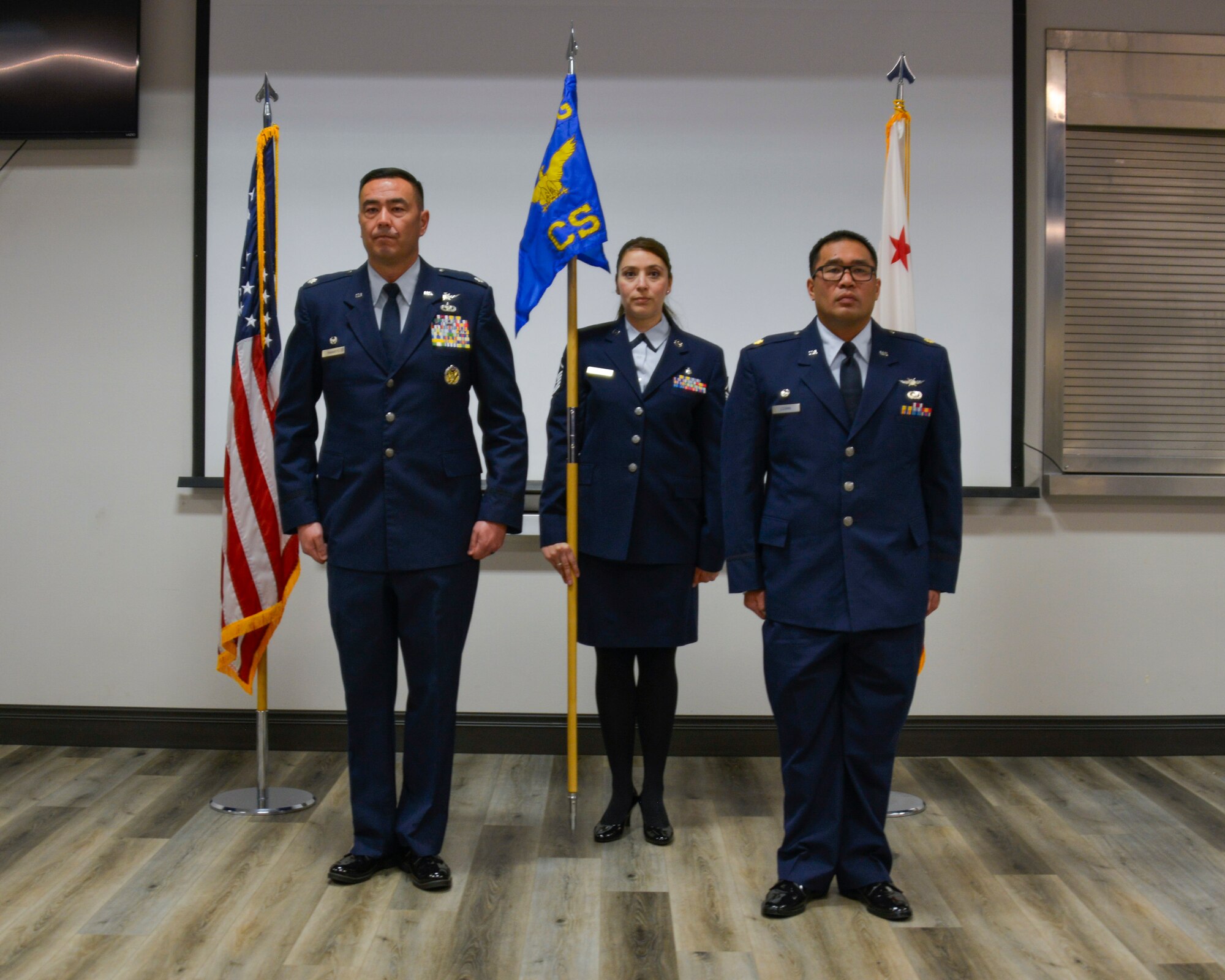 Two male military officers stand beside each other with a space between them. A 1st Sgt. stands about a step behind the two officers in their center holding a guide on.