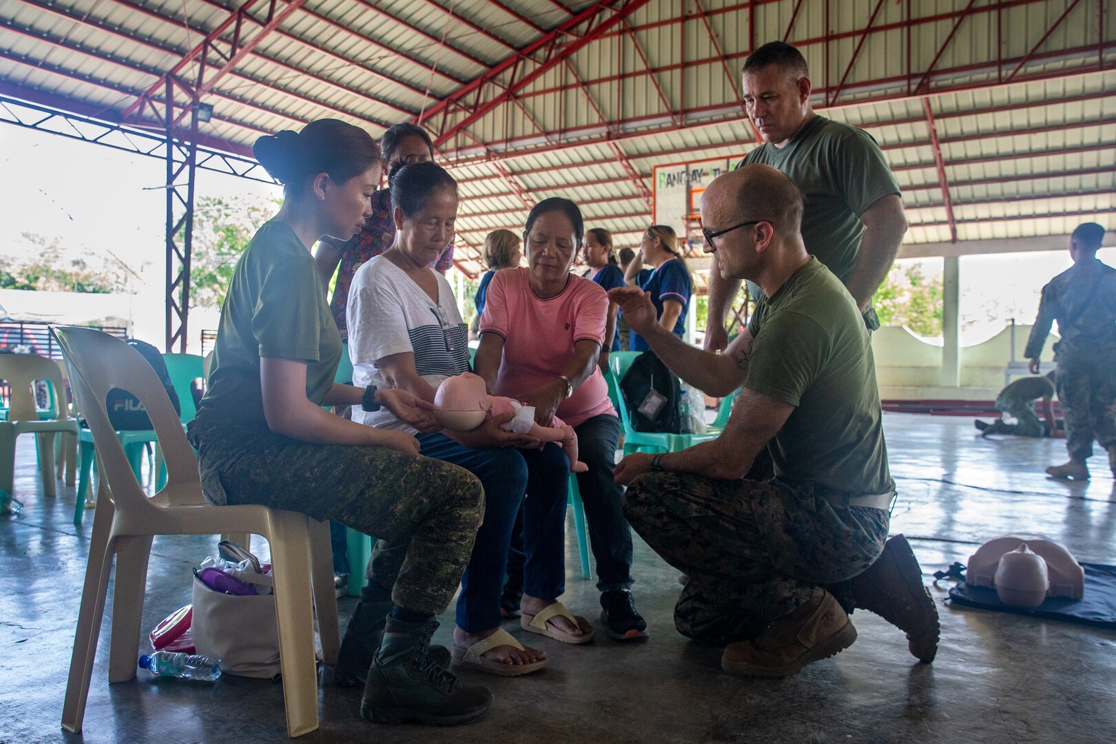 Philippine Army Maj. Johanaville Villanueva, left, a communicable diseases nurse and U.S. Navy Lt. Cmdr. David Loran, a nurse practitioner, guides Ilocos Norte residents applying cardiopulmonary resuscitation on a simulated infant during a community health engagement held before Exercise Balikatan 24 at Davila Elementary School in Pasuquin, Ilocos Norte, Philippines, April 21, 2024. The Philippine and U.S. service members trained Ilocos Norte healthcare workers and residents on basic lifesaving skills such as cardiopulmonary resuscitation and tactical combat casualty care, increasing emergency care access and awareness. BK 24 is an annual exercise between the Armed Forces of the Philippines and the U.S. military designed to strengthen bilateral interoperability, capabilities, trust, and cooperation built over decades of shared experiences. (U.S. Marine Corps photo by Cpl. Trent A. Henry)