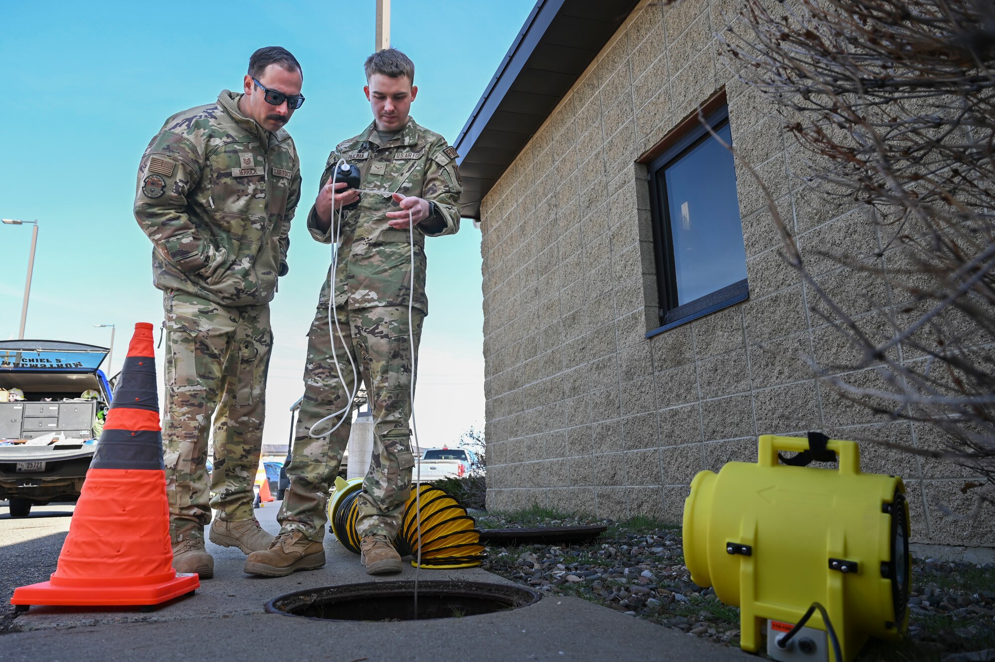 Two people standing next to a manhole with a tube going into the manhole
