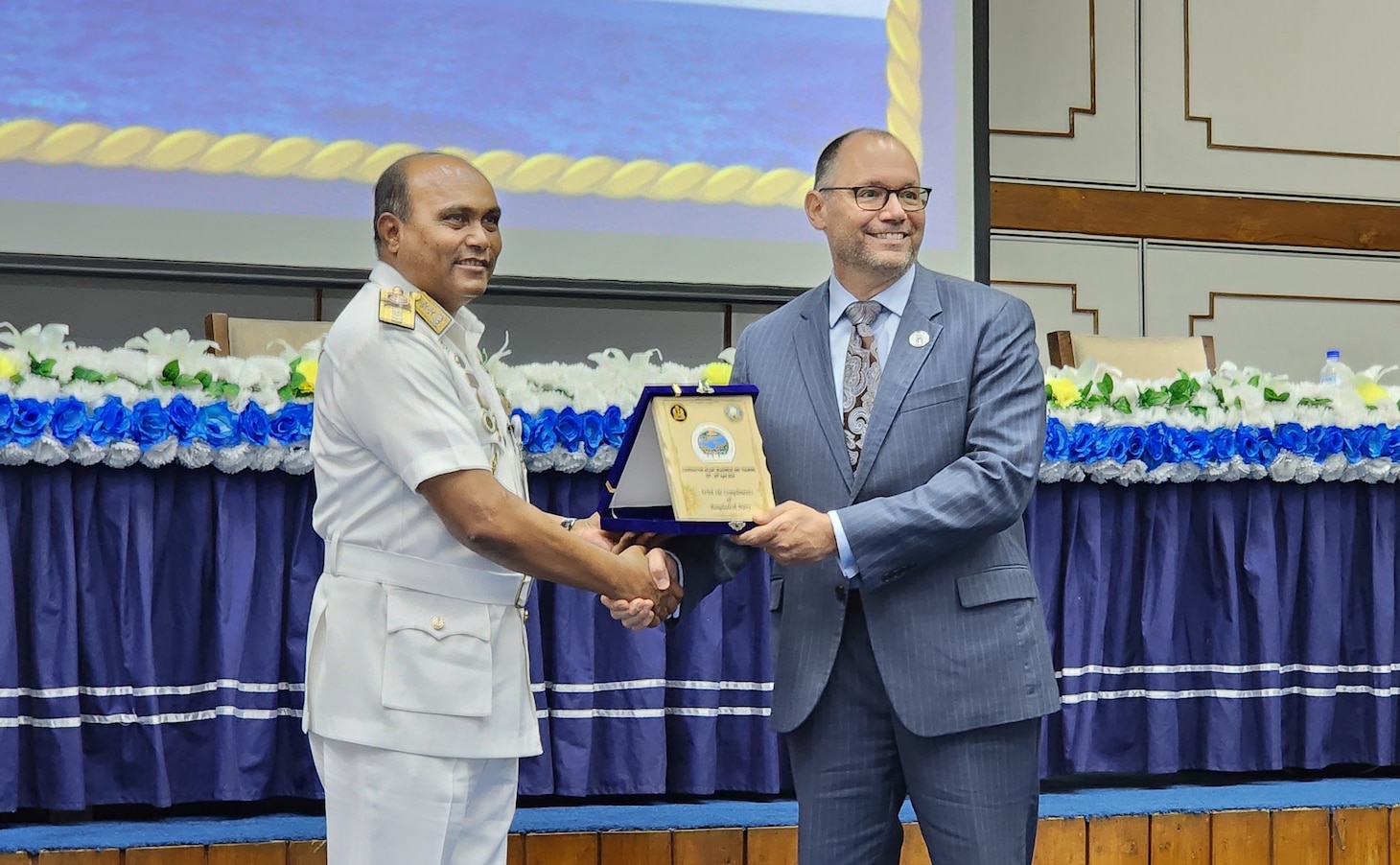 240422-N-NR876-1939 CHATTOGRAM, Bangladesh (April 22, 2024)- Bangladesh Navy head of delegation Rear Adm. Mohammad Anwar Hossain, left, presents a plaque to the U.S. Ambassador to Bangladesh, Mr. Peter Haas during the opening ceremony of Cooperation Afloat Readiness and Training (CARAT) Exercise Bangladesh 2024. CARAT Bangladesh is a week-long exercise that seeks to enhance collaboration focused on shared maritime security challenges in the region. As the 30th iteration of the Cooperation Afloat Readiness and Training (CARAT) series, 2024 highlights the longstanding role of CARAT as a credible venue for regional Allies and partners to address shared maritime security priorities.