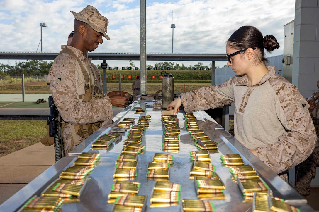 Marines standing on opposite sides count ammunition laid on a silver table with a bridge in the background.