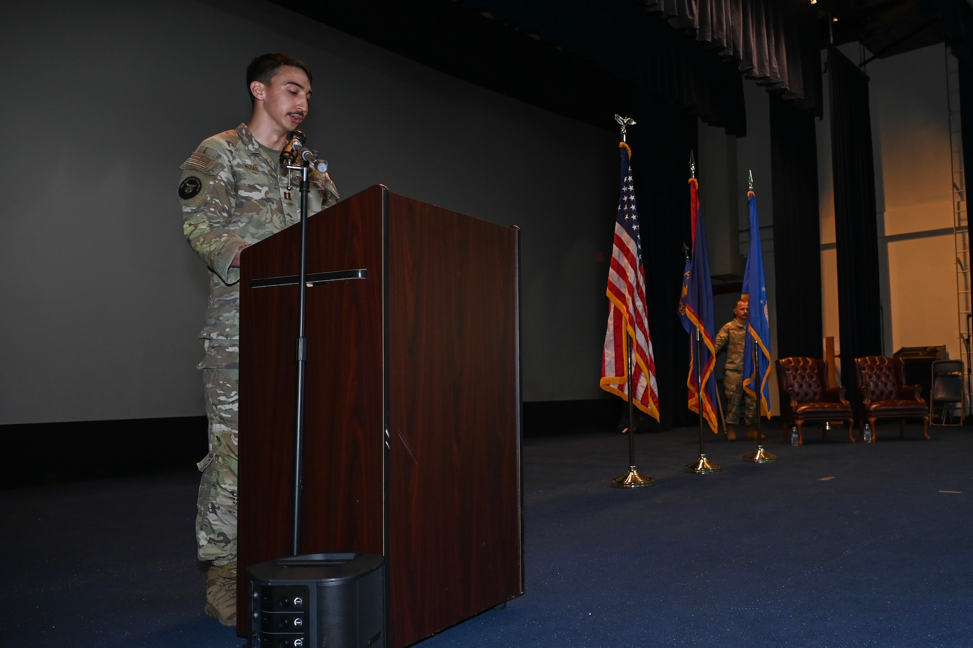 An Airman stands on the stage behind a podium and speaks to the audience.