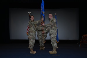 Two Air Force commanders holds a guidon and smile for a photo on stage.