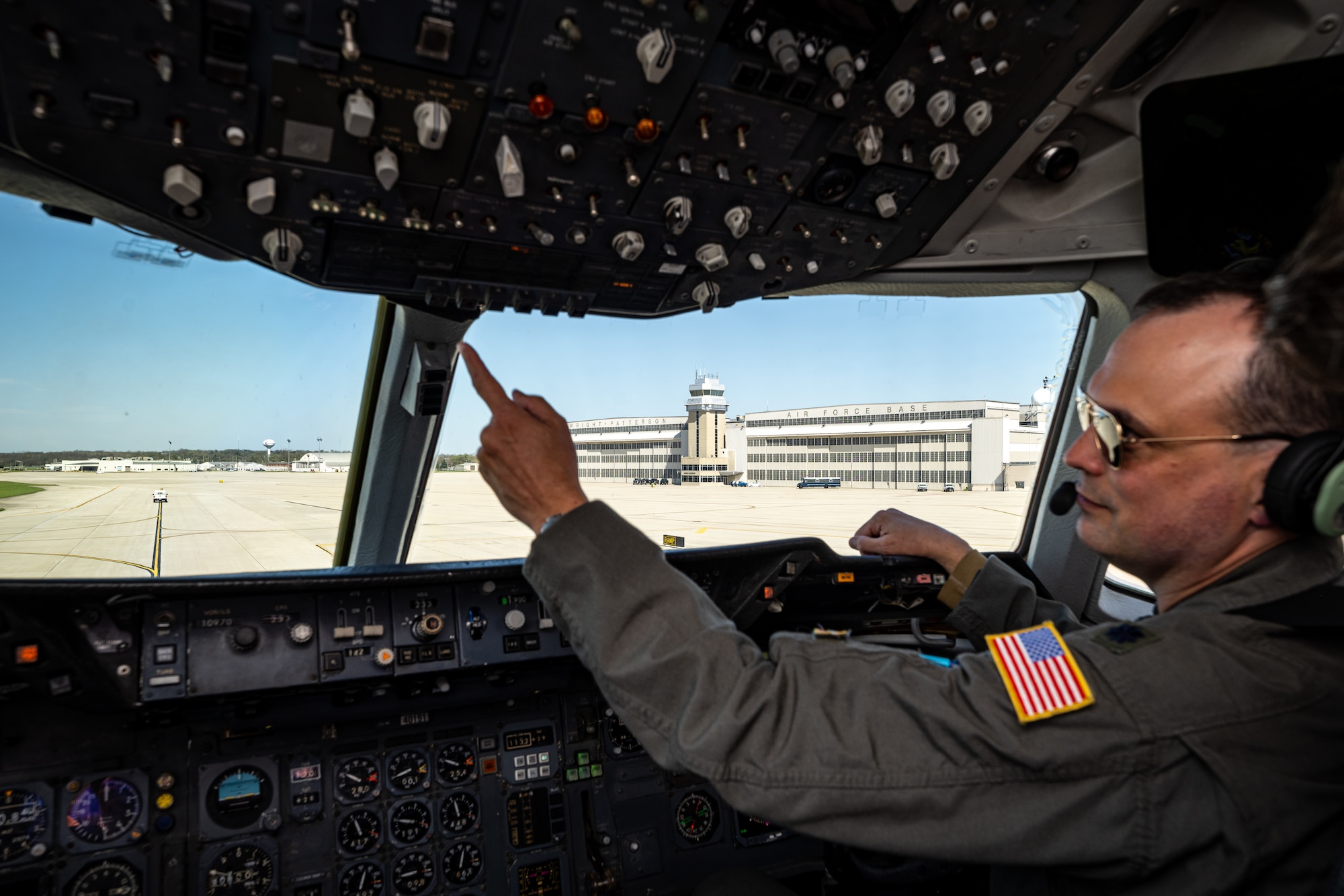 Pilot Lt Col Johnson reaches to press a button inside the cockpit with Wright-Patterson AFB hangars and tower in the background