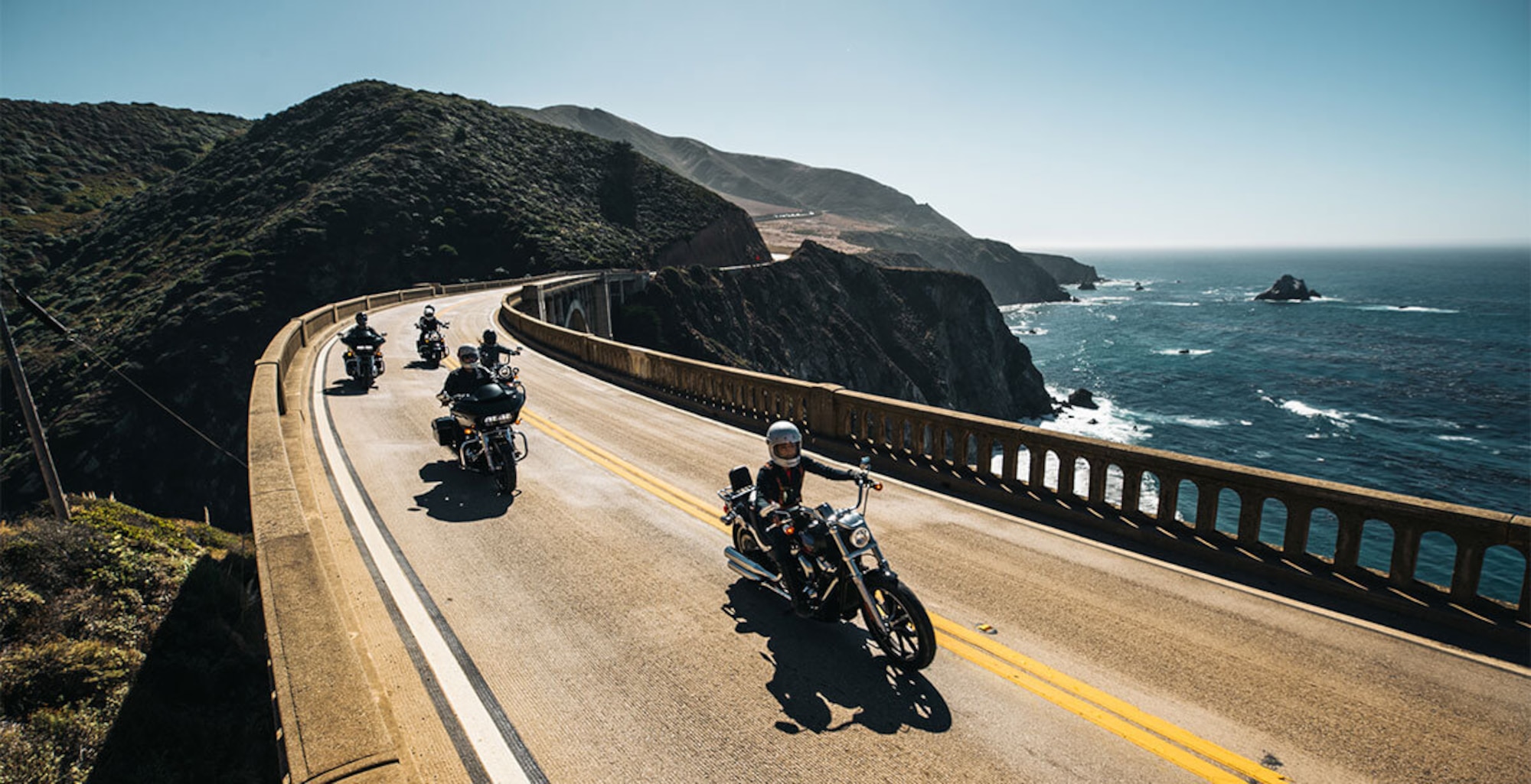 Photo with 4 motorcycle riders driving down a road along the California coast.
