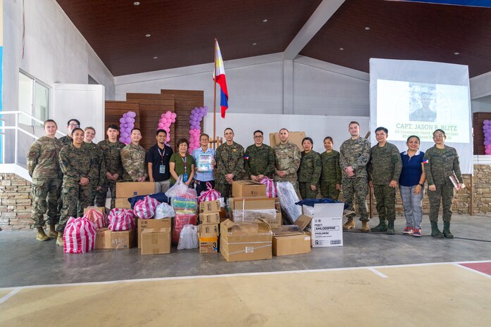 Philippine and U.S. service members with the Combined Joint Civil-Military Operations Task Force, alongside members of the community, pose for a photograph behind donated medical, dental, and office supplies during a community health engagement held before Exercise Balikatan 24 at the Dingalan Municipal Gymnasium in Dingalan, Aurora, Philippines, April 5, 2024. The donated supplies included pallets of medicine, mosquito nettings, dental tools, a CPR mannequin, and more. BK 24 is an annual exercise between the Armed Forces of the Philippines and the U.S. military designed to strengthen bilateral interoperability, capabilities, trust, and cooperation built over decades of shared experiences. (U.S. Marine Corps photo by Cpl. Trent A. Henry)