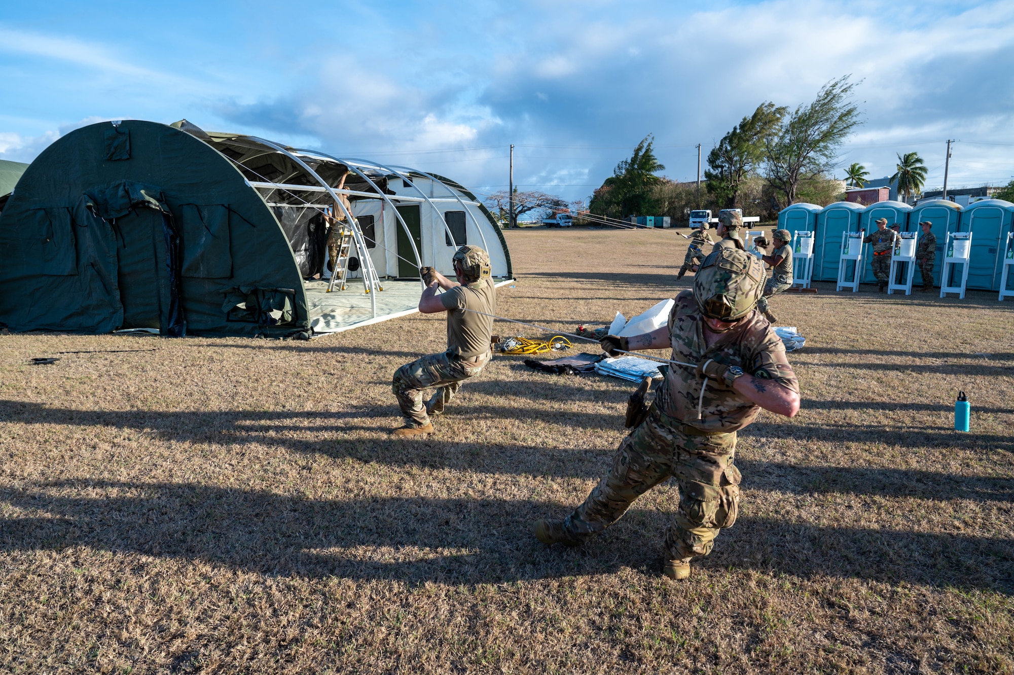 Airmen pull tarp over large tent.