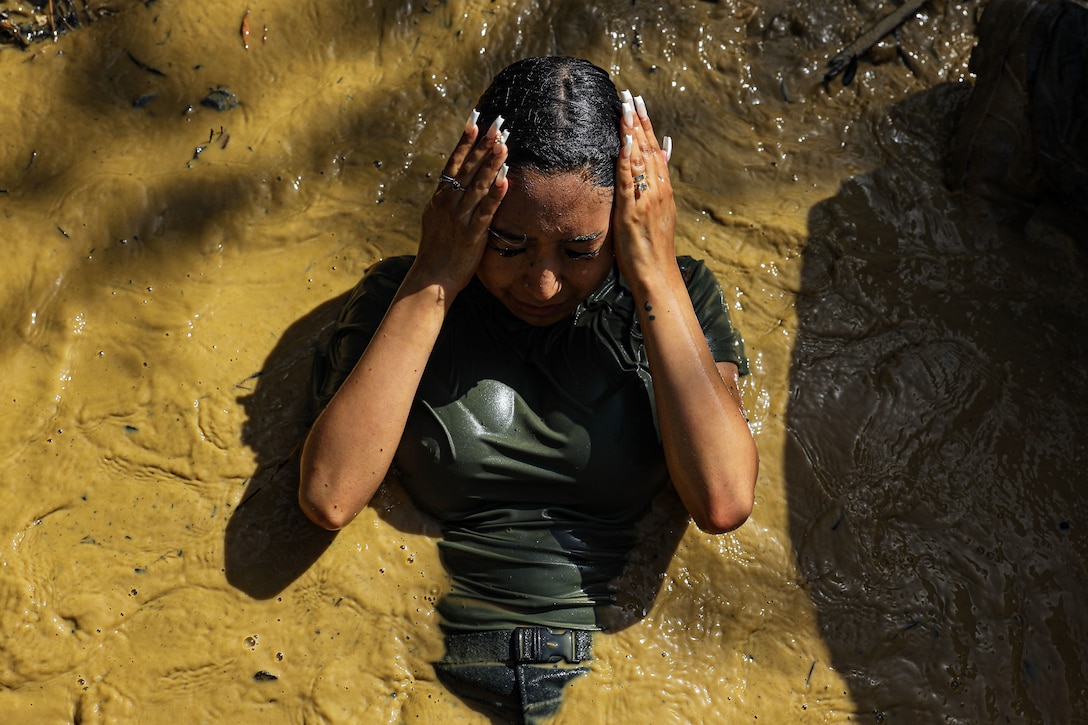 A civilian holds both hands to head while partly submerged in muddy water.