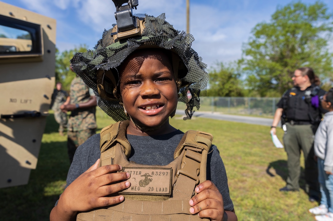 A student at Oaks Road Academy poses for a photo next to a Joint Light Tactical Vehicle, assigned to 2nd Low Altitude Air Defense (LAAD) Battalion, during a career fair in New Bern, North Carolina, April 19, 2024. 2nd LAAD Battalion and Marine Wing Support Squadron (MWSS) 271 participated in a career fair at Oaks Road Academy to engage with the local community. (U.S. Marine Corps photo by Staff Sgt. Daisha Ramirez)