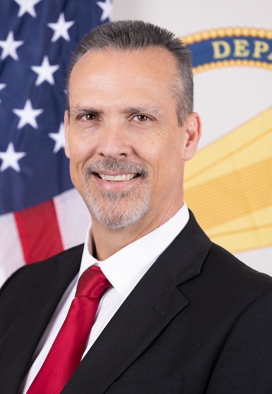 pictured is Mr. Denver S. Heath. He is wearing a black suit, with a white shirt and a red tie. He was selected as the Director of Contracting for the U.S. Army Corps of Engineers (USACE) in February 2024.  He is responsible for leading the USACE contracting activities and overseeing the annual spend of nearly $30B across Military, Civil Works, Environmental, Emergency Operations, and Research and Development missions.