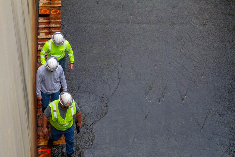 Three men in hardhats stand in shallow water.