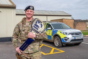An Airman smiles for a photo while holding a “DEFENSOR FORTIS” championship belt