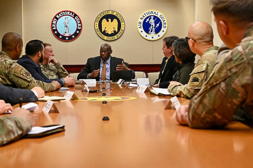 Uniformed service members and people in business attire sit around a conference table.