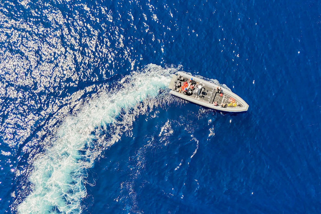 Sailors ride in a small inflatable boat as it creates a wake in a body of water as seen from above.