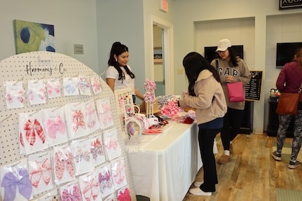 An entrepreneur stands at a table with handmade goods, while others browse the items for sale.