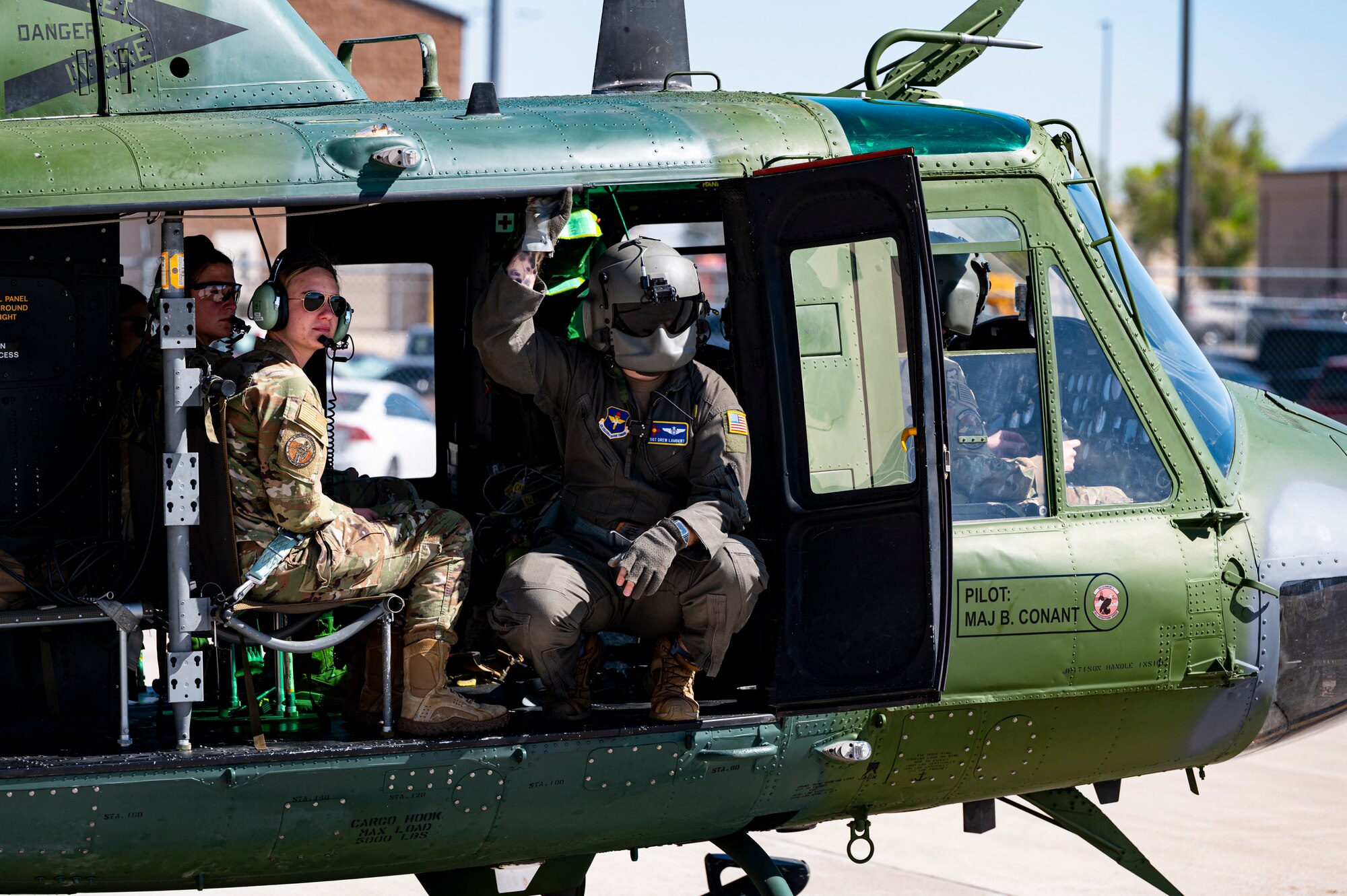 Man stands at edge of a UH-1N helicopter as it prepares to take off.