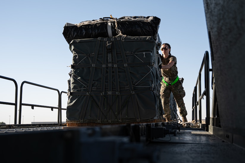Service members in uniform push a pallet of humanitarian assistance onto a military cargo plane.