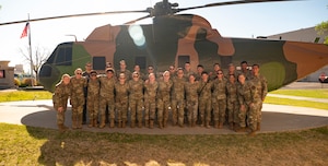 A group poses for a photo in front of a helicopter.