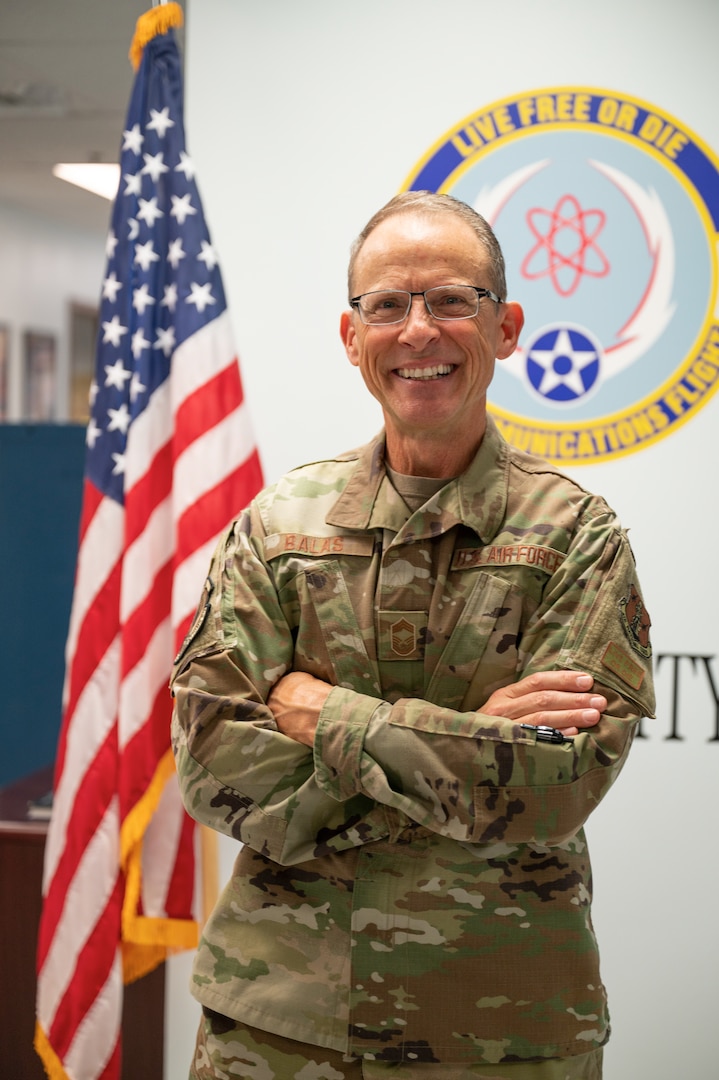 Chief Balas stand in front of the Communications Squadron Logo