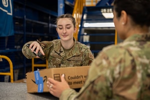 U.S. Air Force Airman 1st Class Brooke Garrison, 51st Force Support Squadron military postal clerk, scans a package while assisting a customer at Osan Air Base, Republic of Korea, April 19, 2024. The Osan AB Postal Office operates as an extension of the United States Postal Service, providing postal services to service members, dependents, and Department of Defense civilians overseas during both normal and contingency operations. Garrison has been an asset to the team, going above and beyond, earning her the title of Mustang of the Week. (U.S. Air Force photo by Staff Sgt. Aubree Owens)
