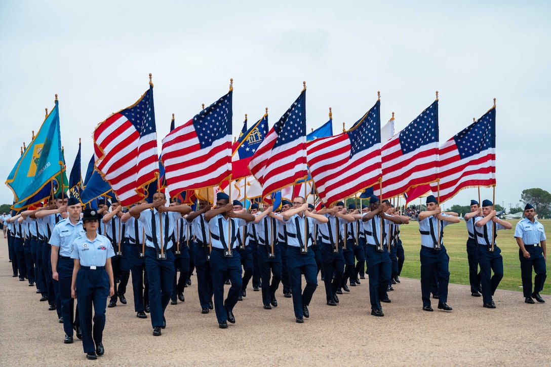 Airmen carrying flags march in formation.