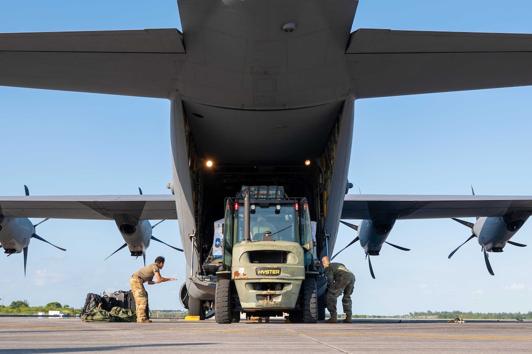 Service members use a vehicle to load pallets into the cargo hold of a large aircraft.