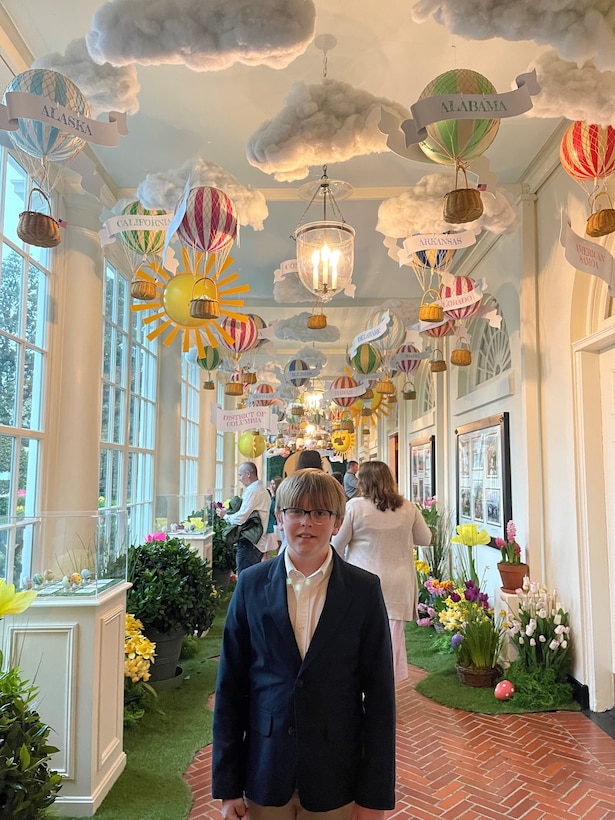 Eli Willingham, son of Sgt. 1st Class Vincent Willingham, readiness Non-commissioned officer for the Headquarters and Headquarters Company, 1792nd Combat Sustainment Support Battalion, stands inside the White House's East Colonnade where his egg design that he submitted to the White House for First Lady's Egg Roll is displayed.