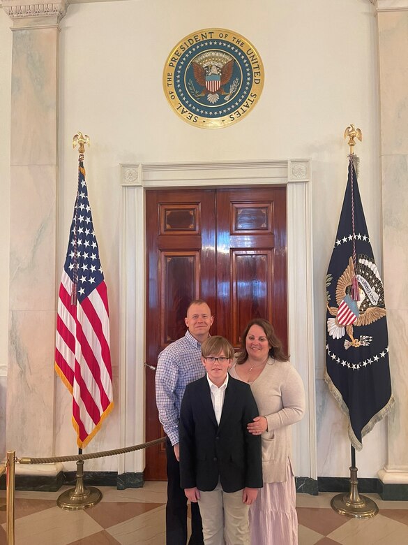 Sgt. 1st Class Vincent Willingham, readiness Non-commissioned officer for the Headquarters and Headquarters Company, 1792nd Combat Sustainment Support Battalion, poses for a photo with his wife and son Eli, inside the White House's East Colonnade where his son's egg design that he submitted to the White House for First Lady's Egg Roll is displayed.