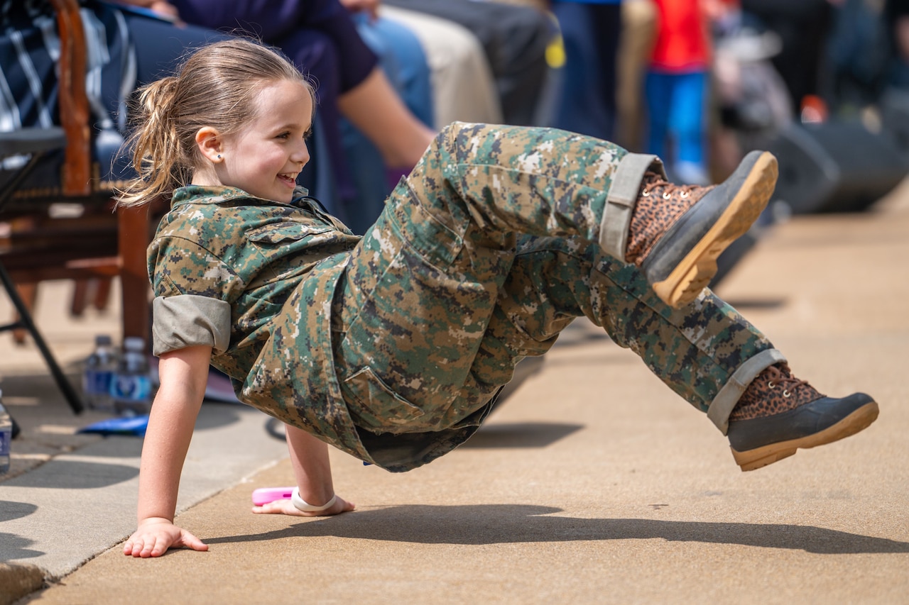 A child in fatigues break dances on the ground.