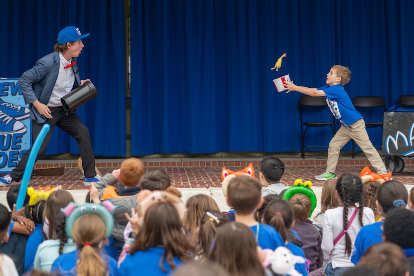 A magician performs on a stage with a child.