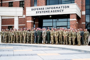 A group of Airmen stand together for a group photo in front of the Defense Information Systems Agency.