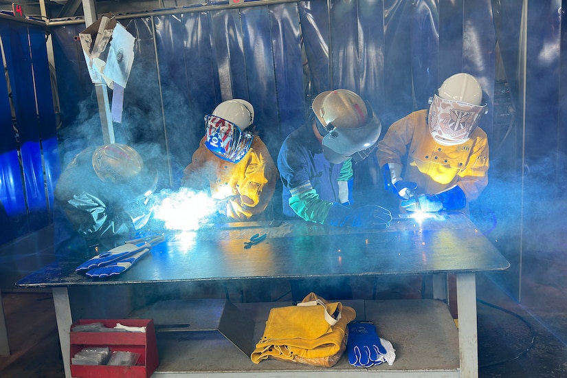 Welders work on the keel of a future ship.