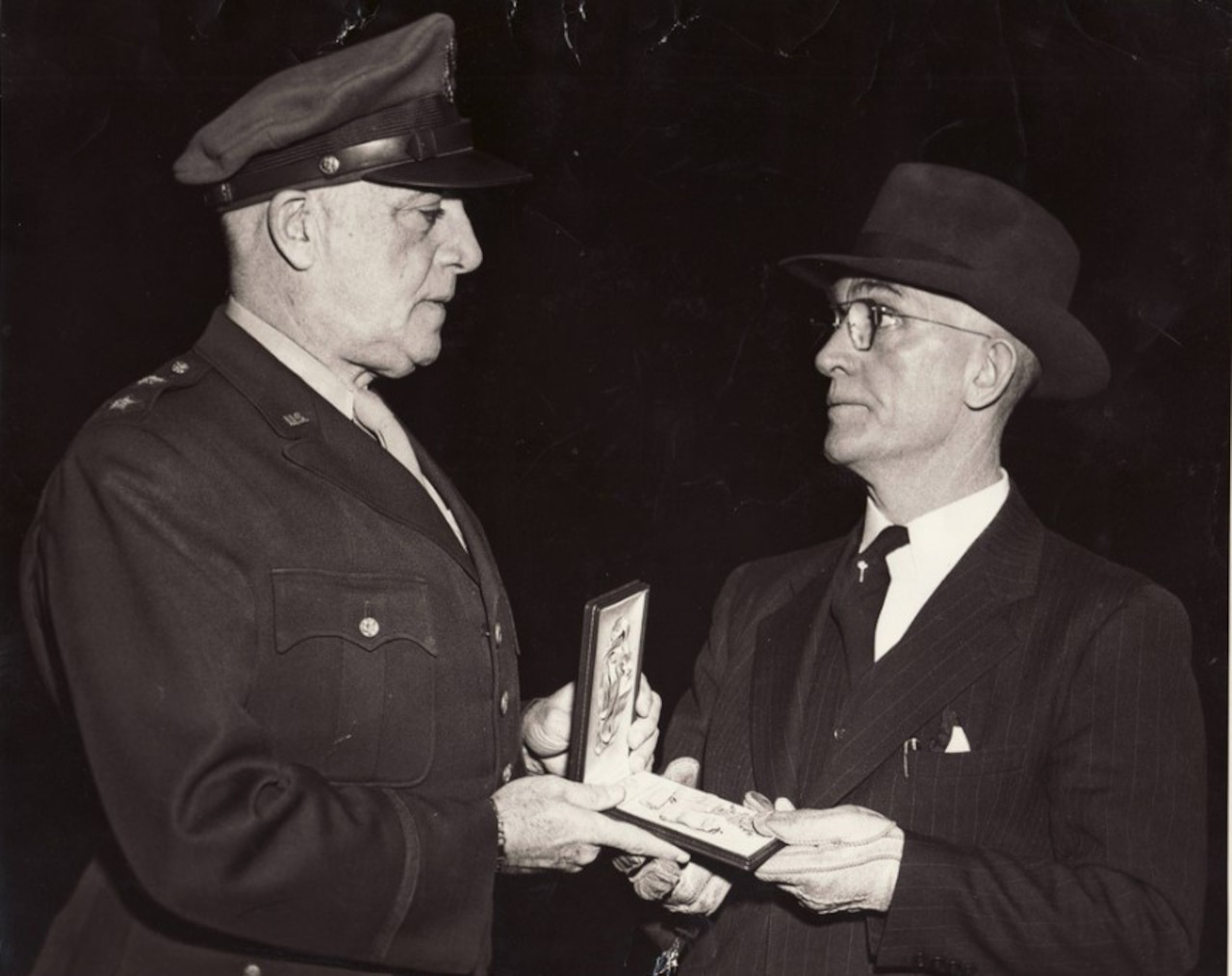 A man hands another man a medal in a box.