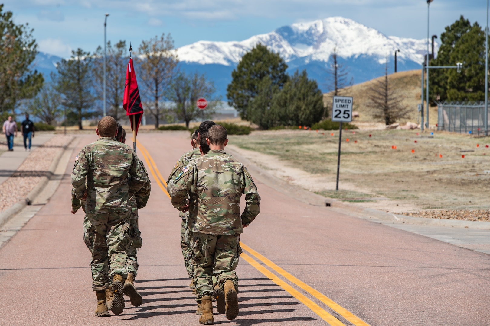 military members in uniform running in formation in front of mountain range