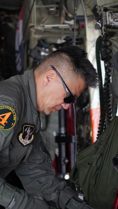 A side profile shot of a MAFFS loadmaster in a green flight suit preparing equipment in the back of a C-130J military aircraft.