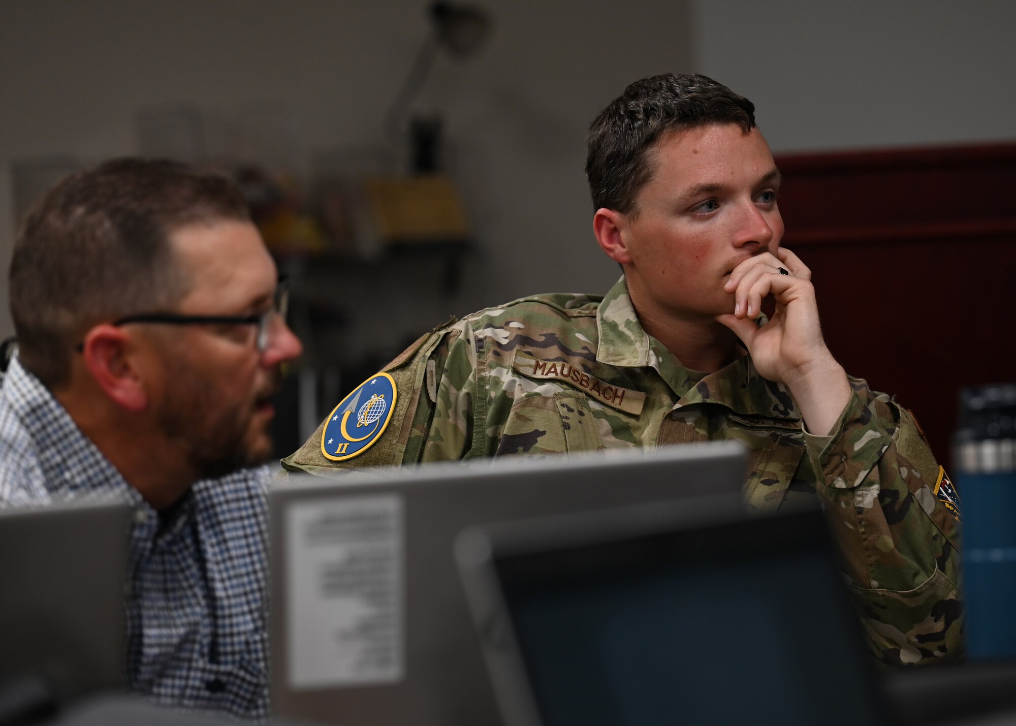 Man sits at desk with a computer listening to his teammate.