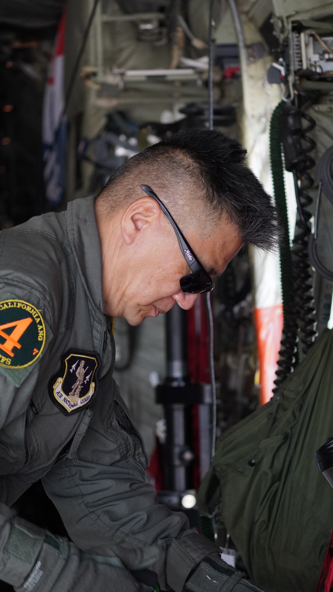 A side profile shot of a MAFFS loadmaster in a green flight suit preparing equipment in the back of a C-130J military aircraft.