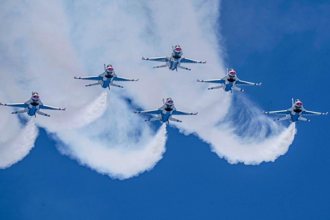 Six military aircraft fly in formation leaving swirling smoke behind them.