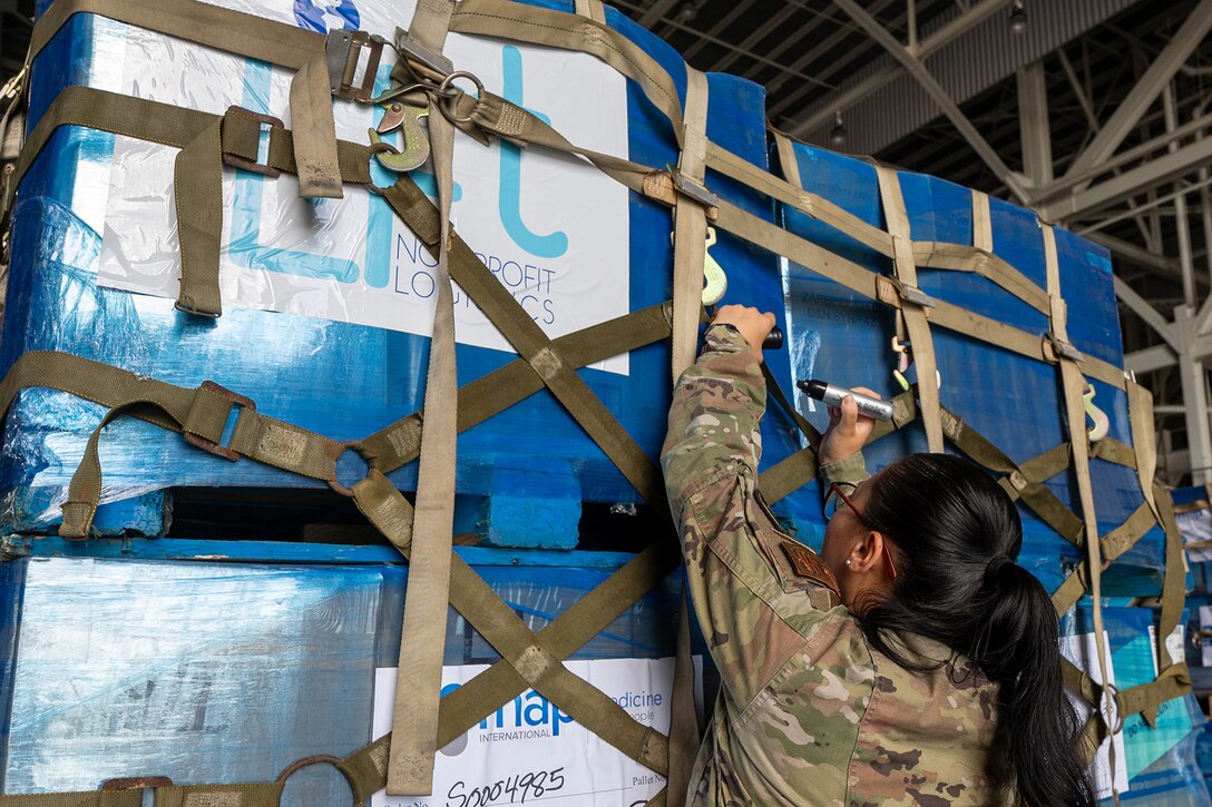 An airman reaches up to write on the side of a box on a strapped pallet of supplies.