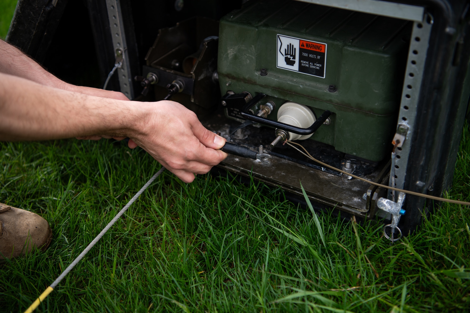 A hand holding a cable, appearing to insert it into a device. In the foreground, grass.