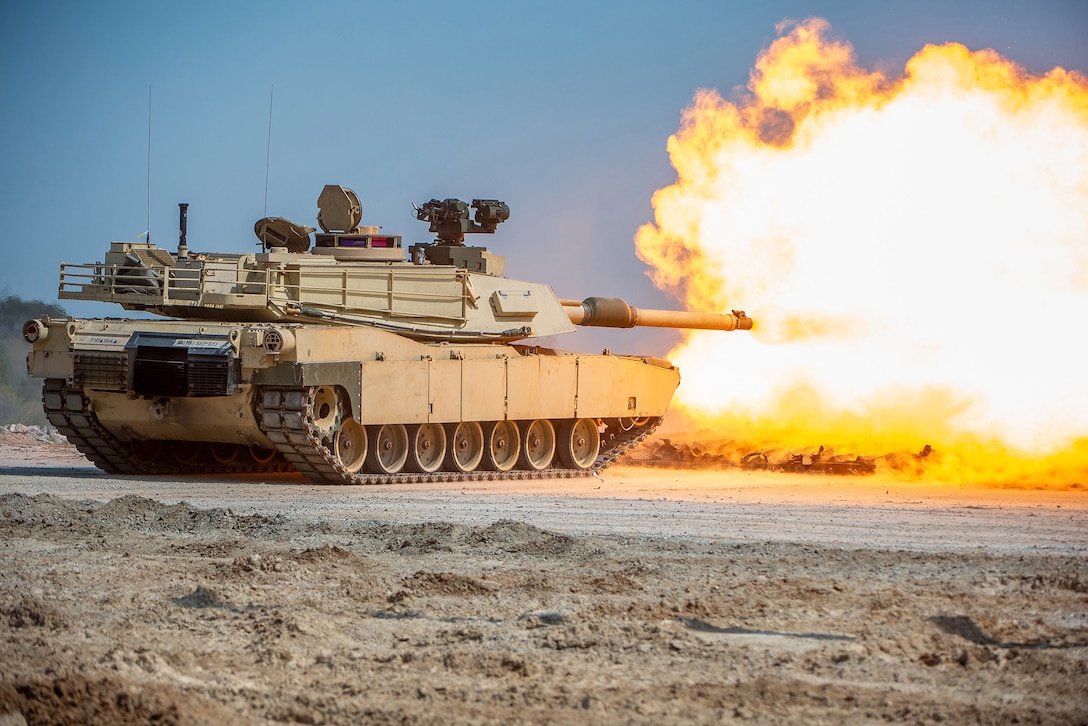 A military tank fires bright orange flames during daylight on a dirt road.