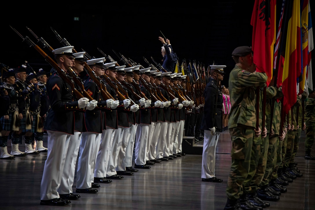 Marines in dress uniform stand in formation during a dress rehearsal for a music event. A row of service members in the front carry various flags.