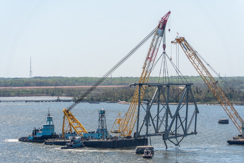 A large floating crane lifts a giant truss of fallen bridge out of the water.